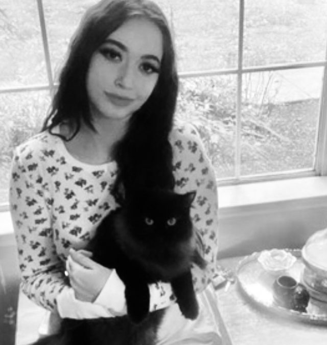 Iris sitting by a window holding her fluffy black cat, Lotus